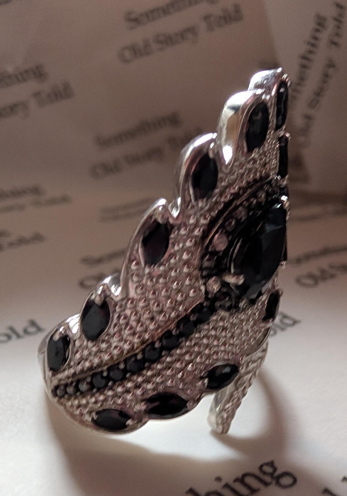 Silver statement ring with a leaf design, set with black gemstones. The ring has a central oval stone and smaller stones around the edges, creating a striking and elegant accessory. __etsy:7769405963