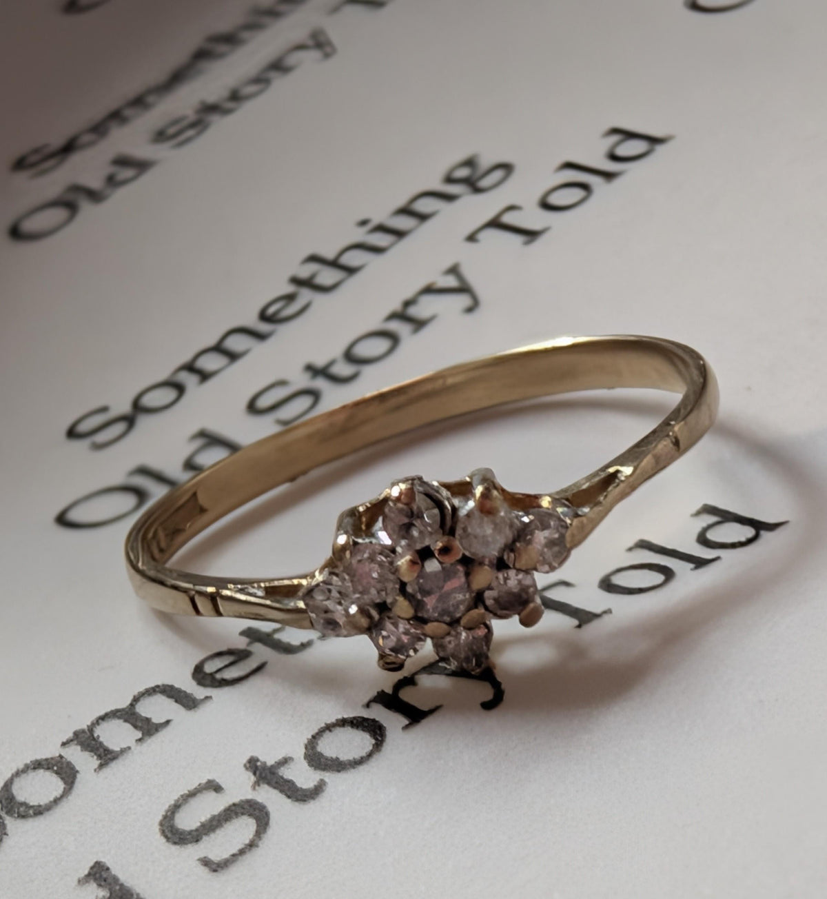A gold ring featuring a cluster of small, clear gemstones. The ring is set against a white background with the words "Something Old Story Told" printed in black. __etsy:7692670456