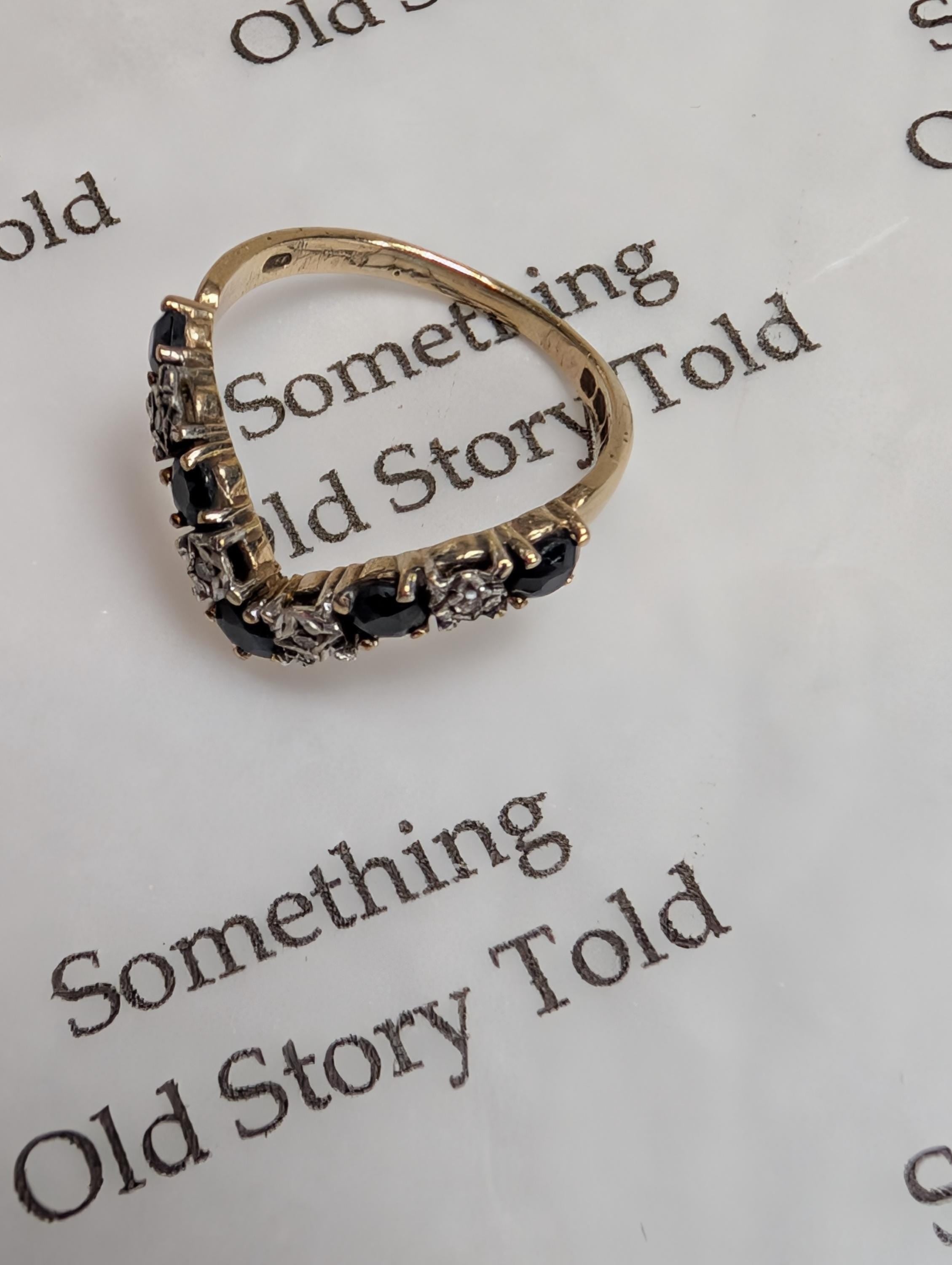A gold ring with a V-shaped design, set with dark blue and clear gemstones. The ring is displayed on a white surface with the text "Something Old Story Told". __etsy:7928172985
