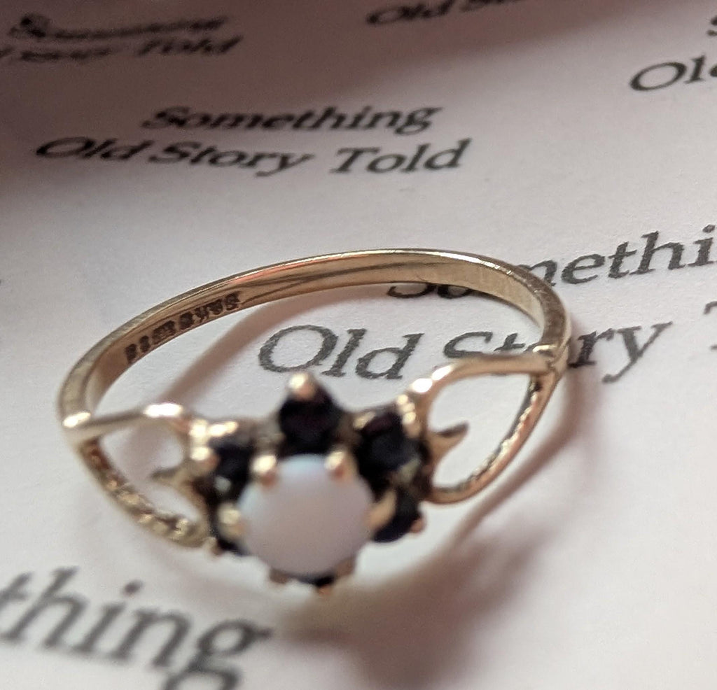 A gold ring featuring a central white gemstone, framed by black stones. The ring's band has an ornate, open design. The word "Romayes" is stamped on the ring. __etsy:7751864512