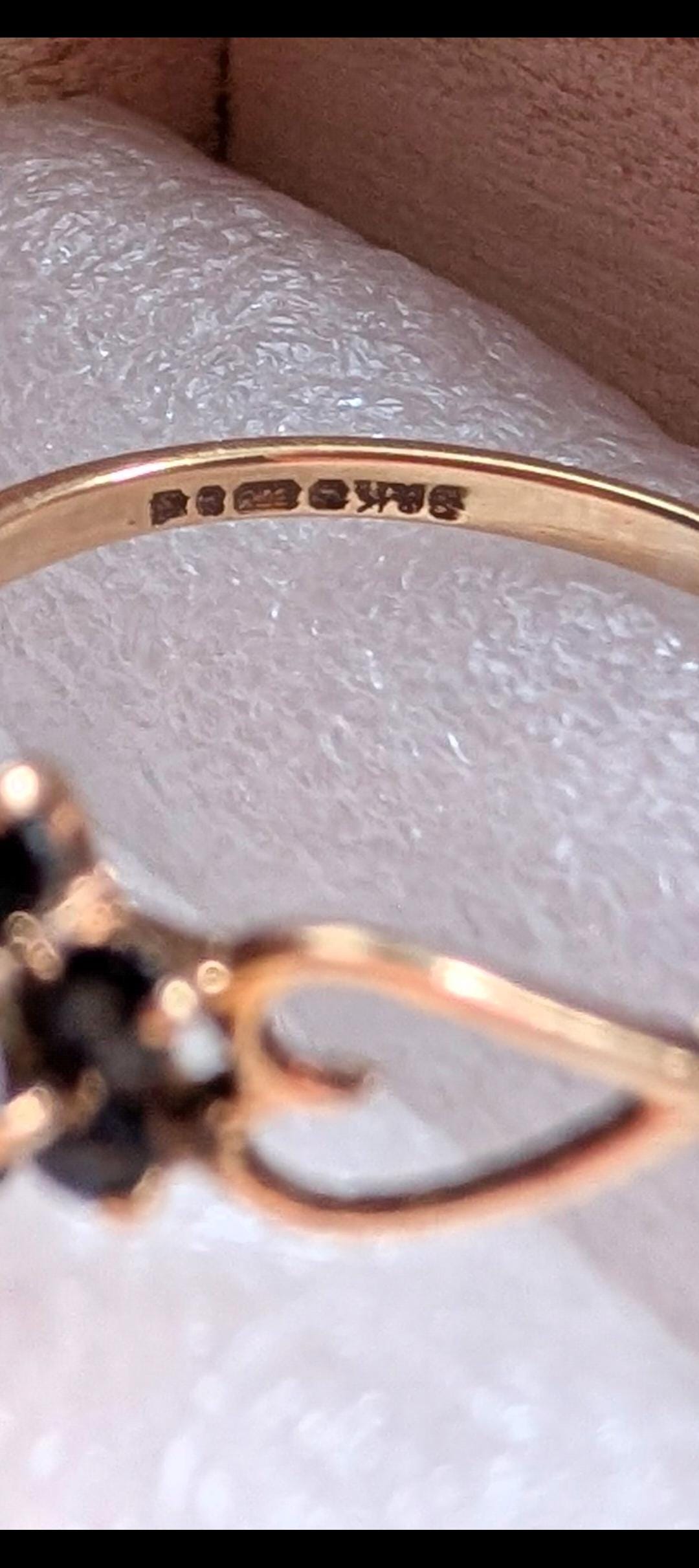 Close-up of a gold ring with a dark gemstone. The ring has a delicate design with intricate details. The band is stamped with markings, indicating its quality. The ring is set against a soft, white background. __etsy:7751864564