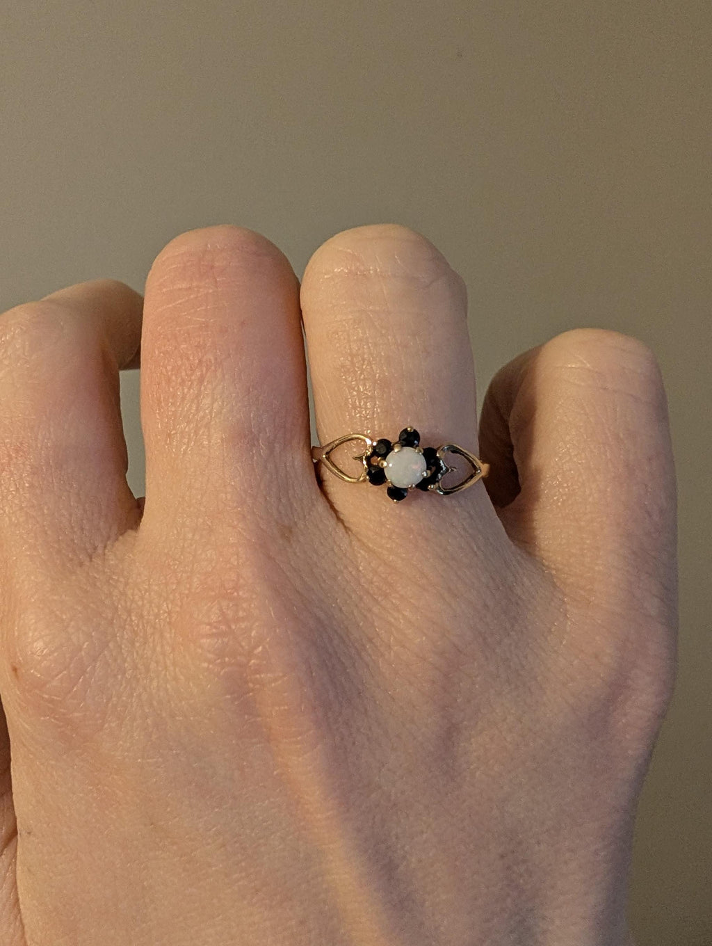 A gold ring with a floral design, featuring a central white stone and surrounding black stones. The ring is displayed on a hand, highlighting its intricate details. The ring's band has an open, filigree-like design, showcasing the craftsmanship. __etsy:7751864580